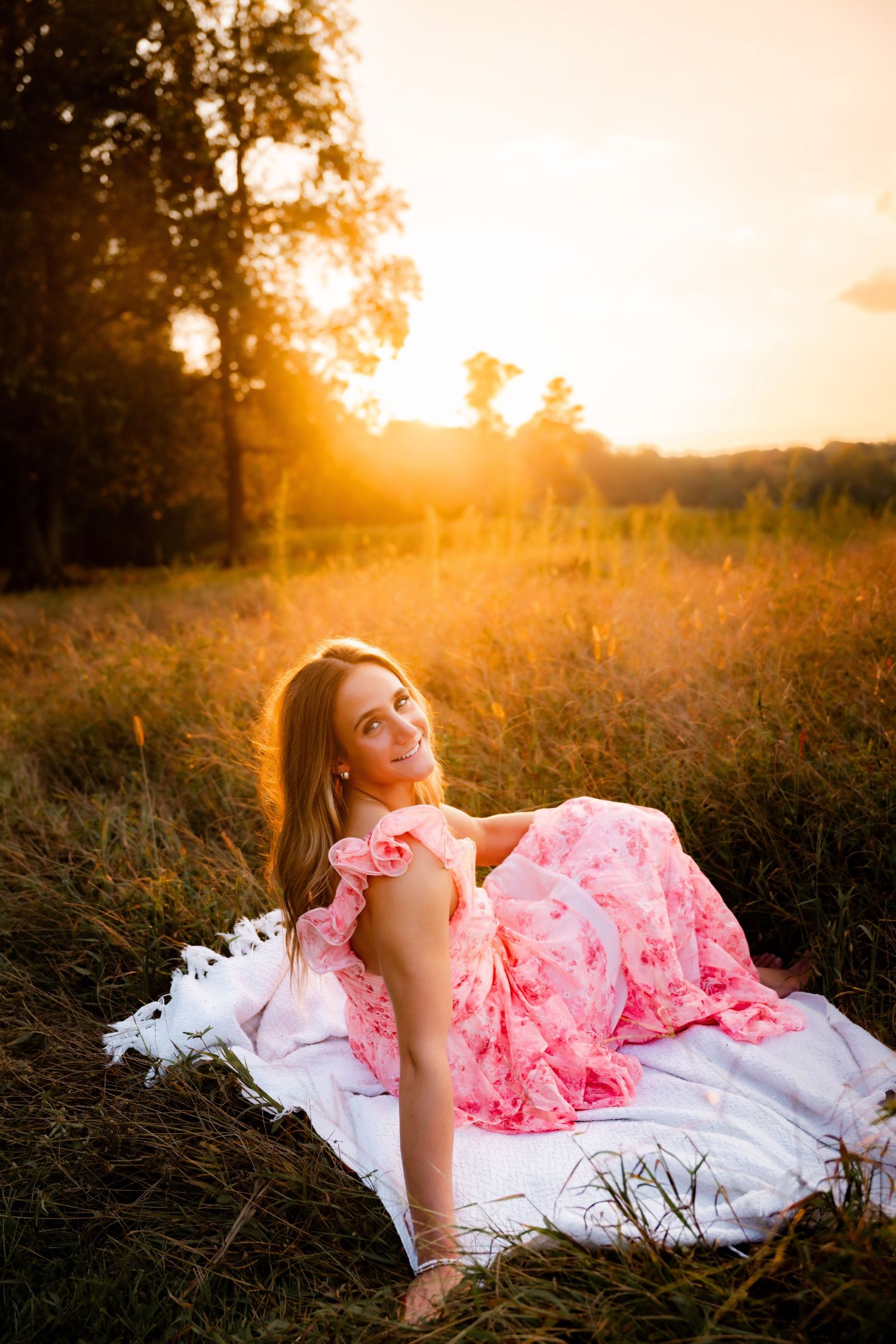 Woman in pink dress reclining on white blanket during golden hour.