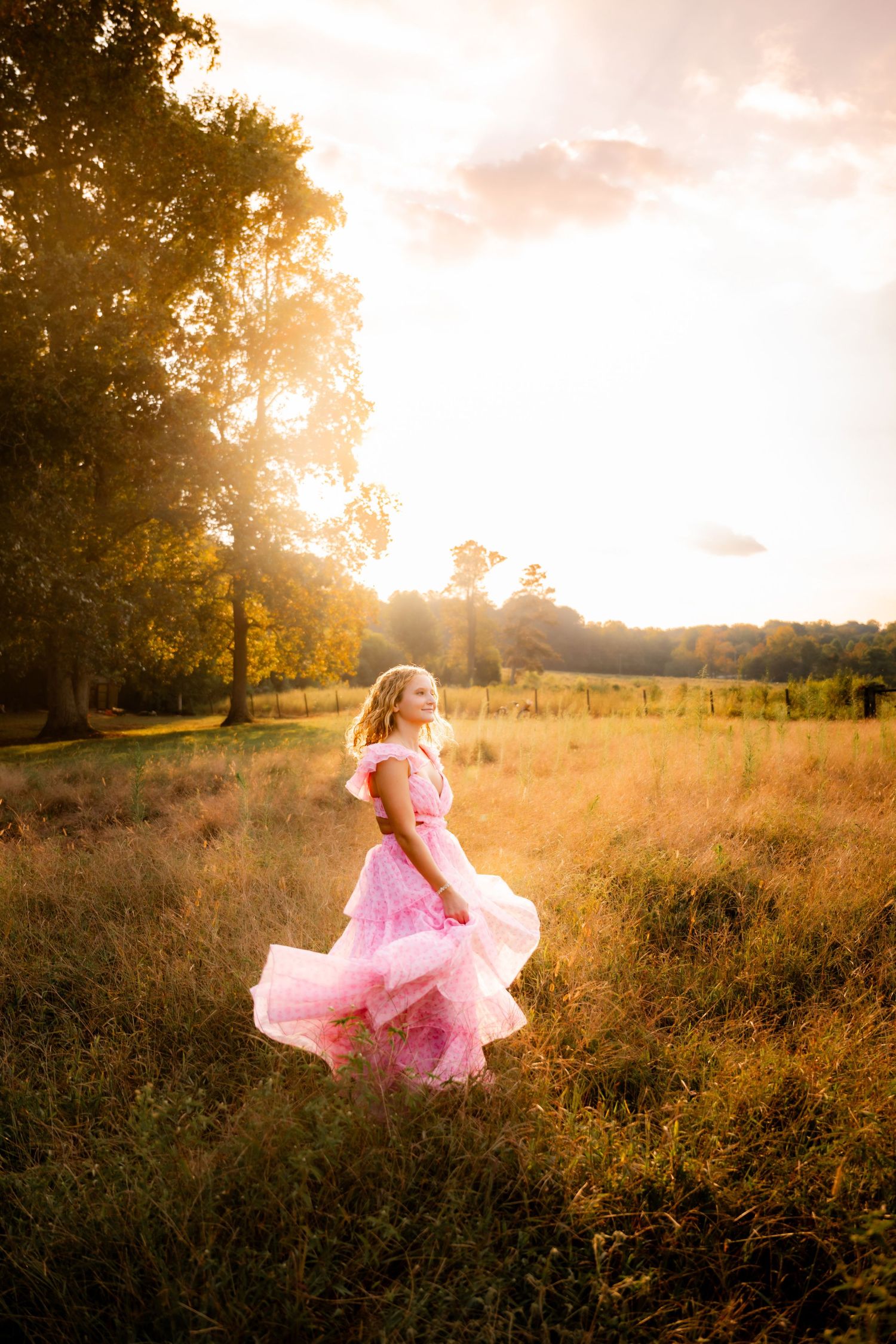 Woman in flowing pink dress twirling in field at sunset.