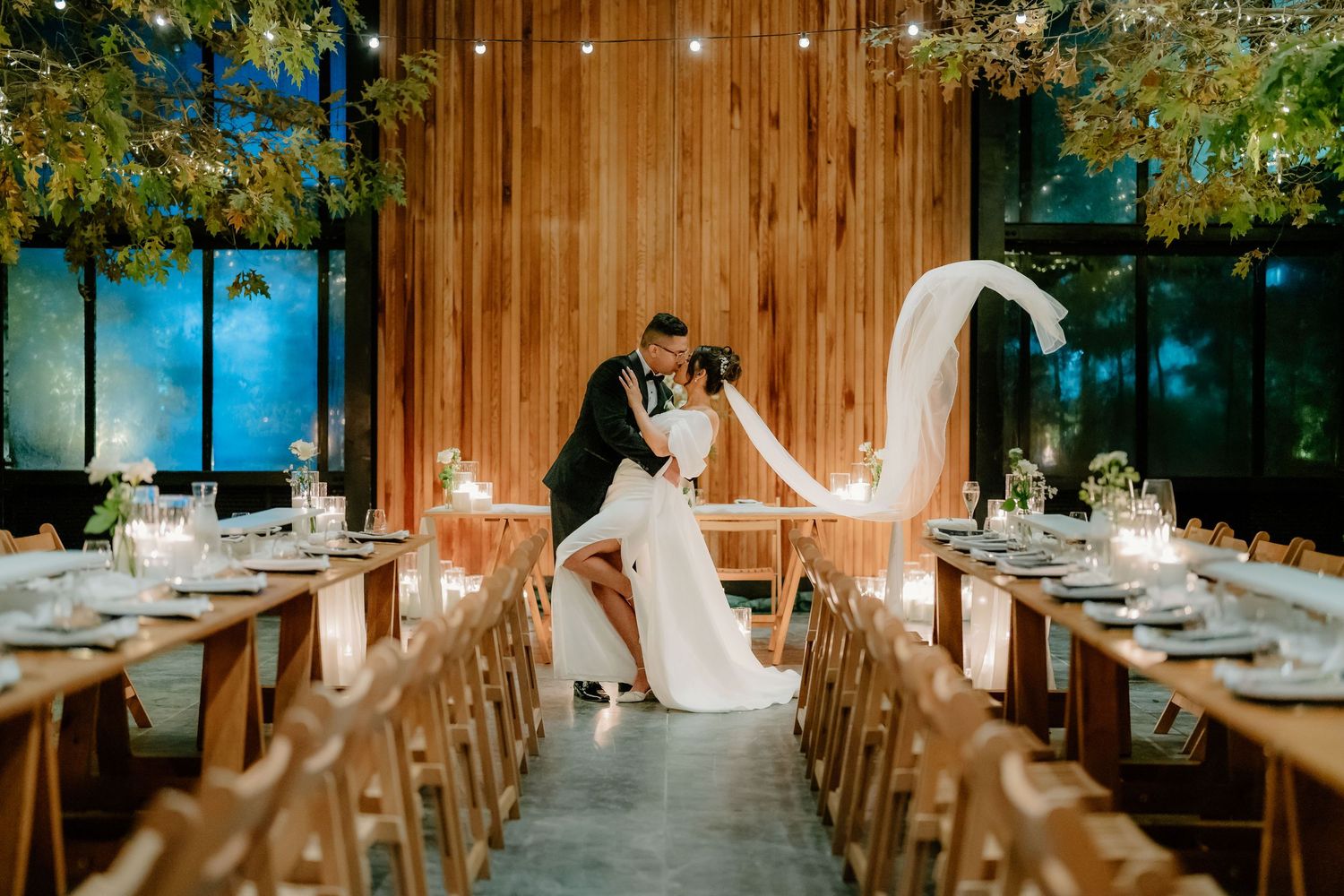 A romantic wedding reception setup in a rustic wooden venue with elegant table settings and soft glowing candlelight.