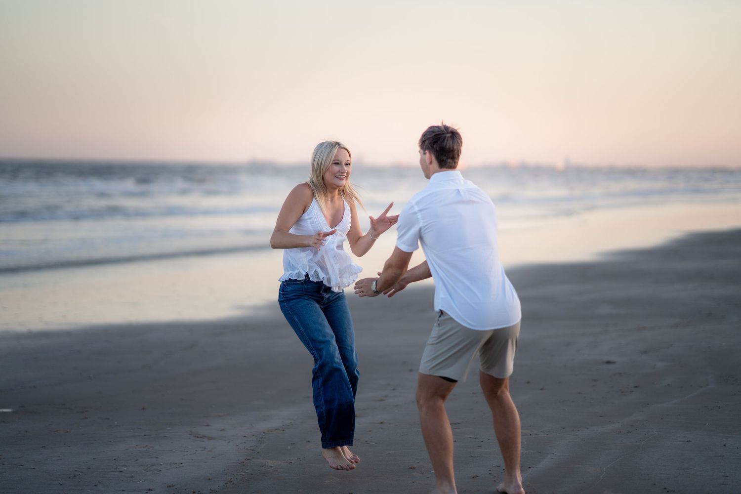 Woman in white dress dancing joyfully on a sunny beach with ocean waves, embodying freedom and happiness.