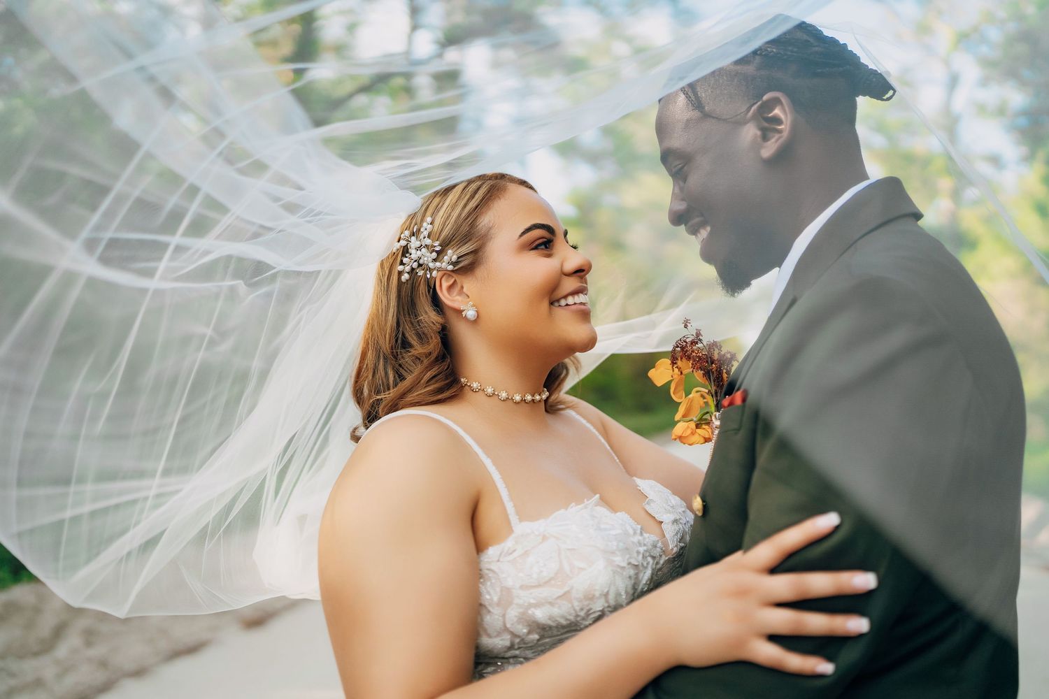 A joyful outdoor wedding moment with flowing veil, lace gown and orange boutonniere.