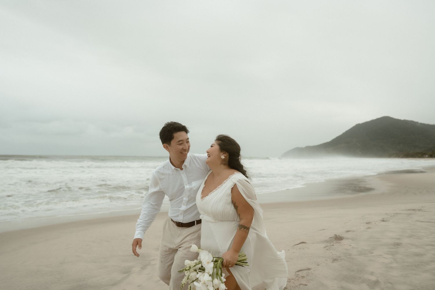 A romantic beach wedding moment captured against a misty coastal backdrop.