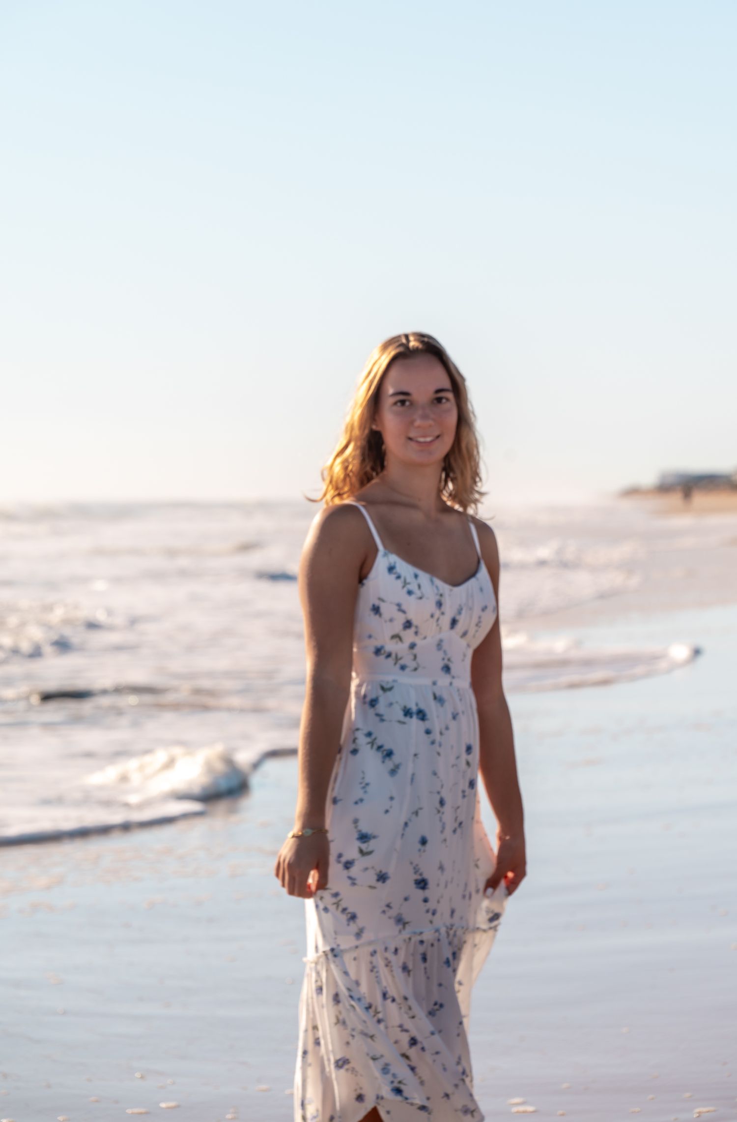 A person in a flowy white sundress stands in a meadow of wildflowers surrounded by lush greenery.