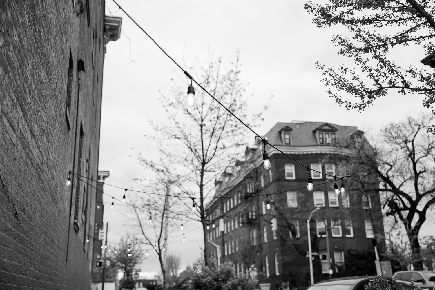 A black and white urban street view showing a brick apartment building with dormers and utility lines overhead.