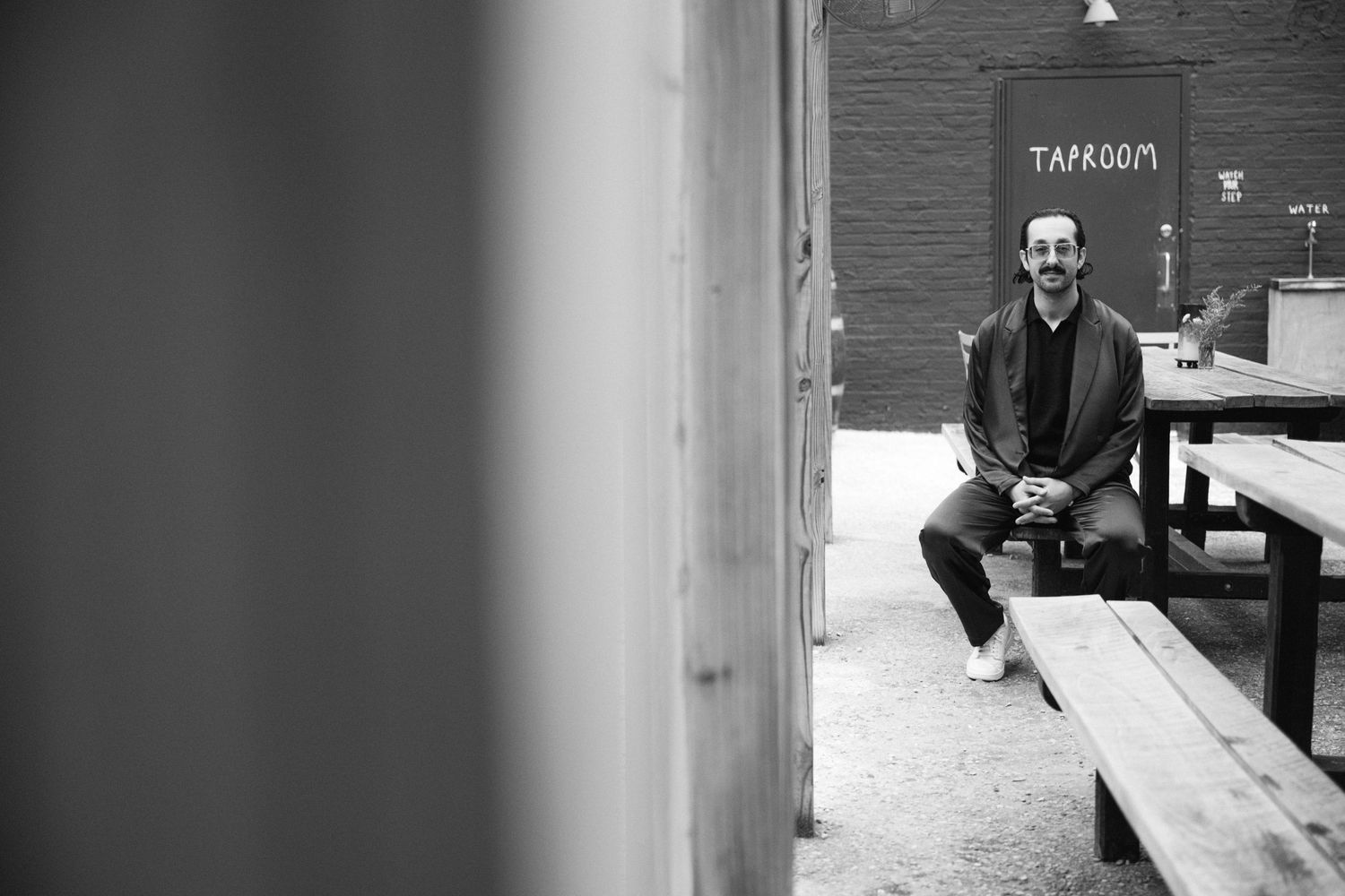 A black and white photo showing someone sitting casually on wooden steps outside a building.