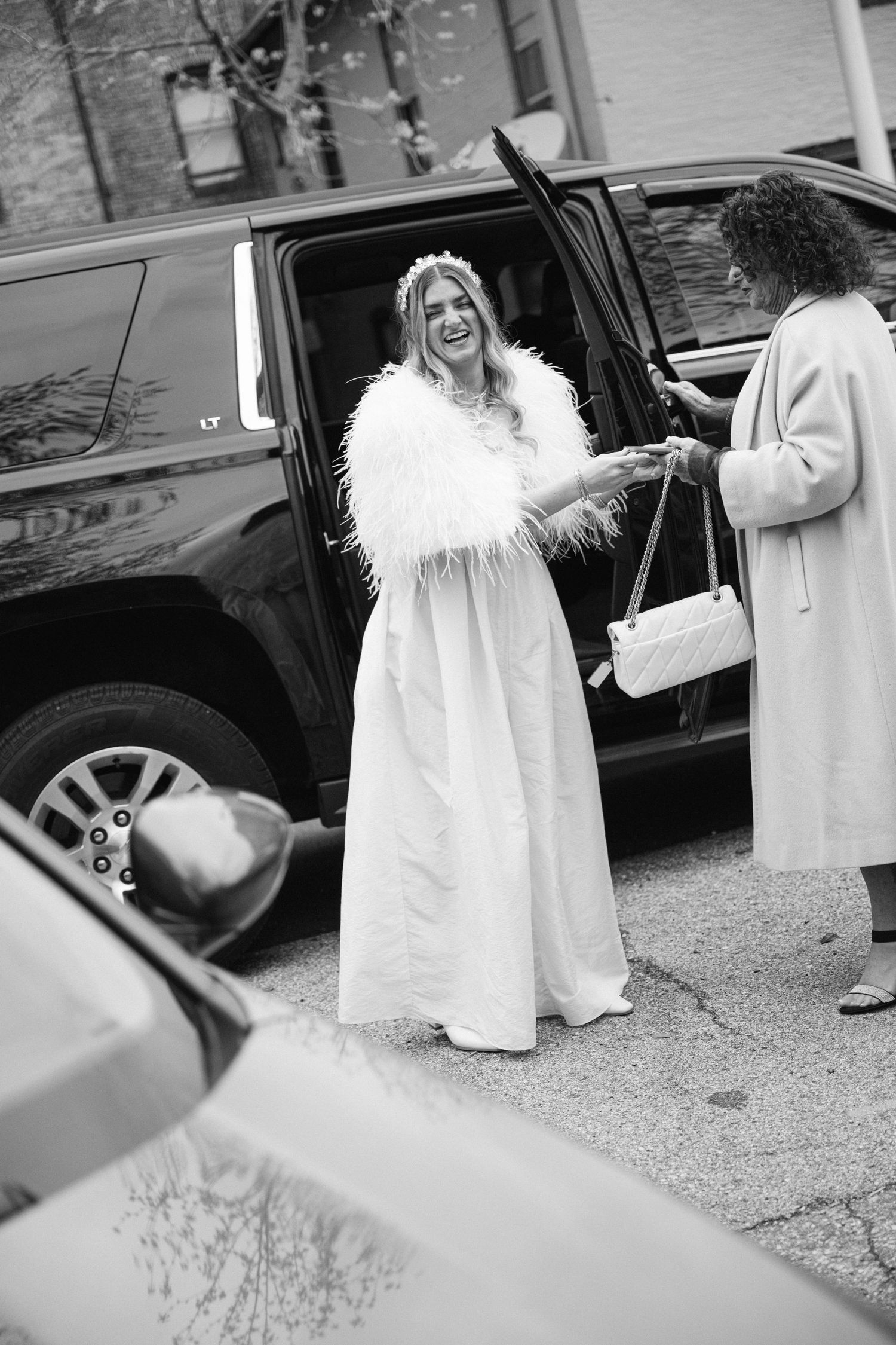 Two people in white outfits sharing a joyful moment next to a black car on the street.