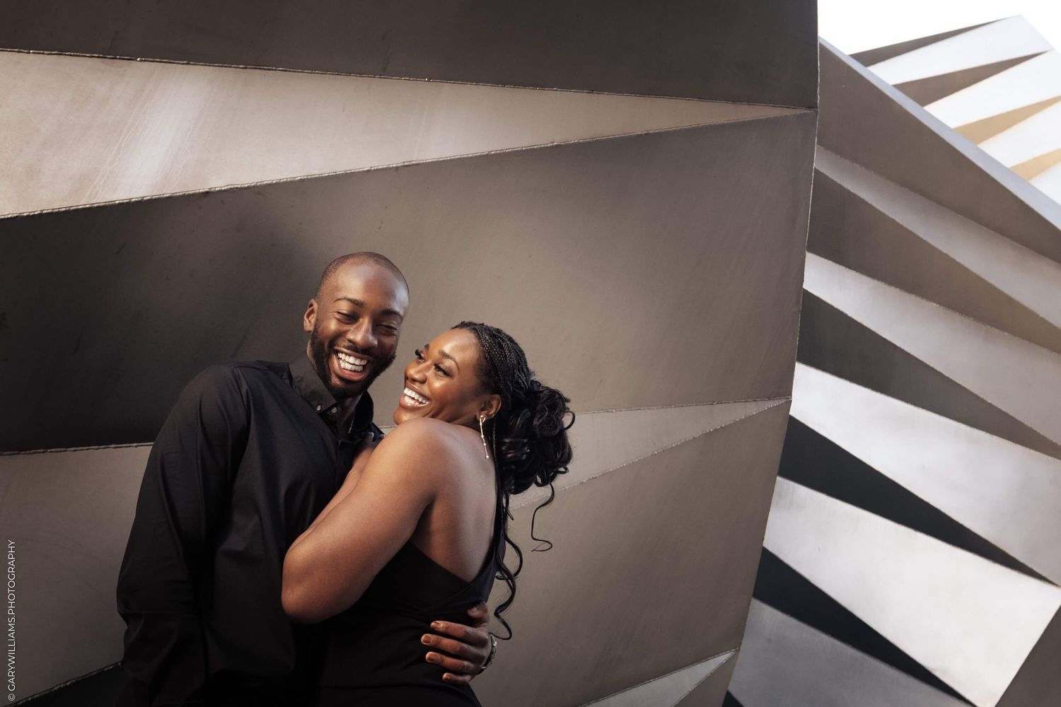 A happy couple shares an intimate moment and laughter together in a modern setting with geometric wall details.