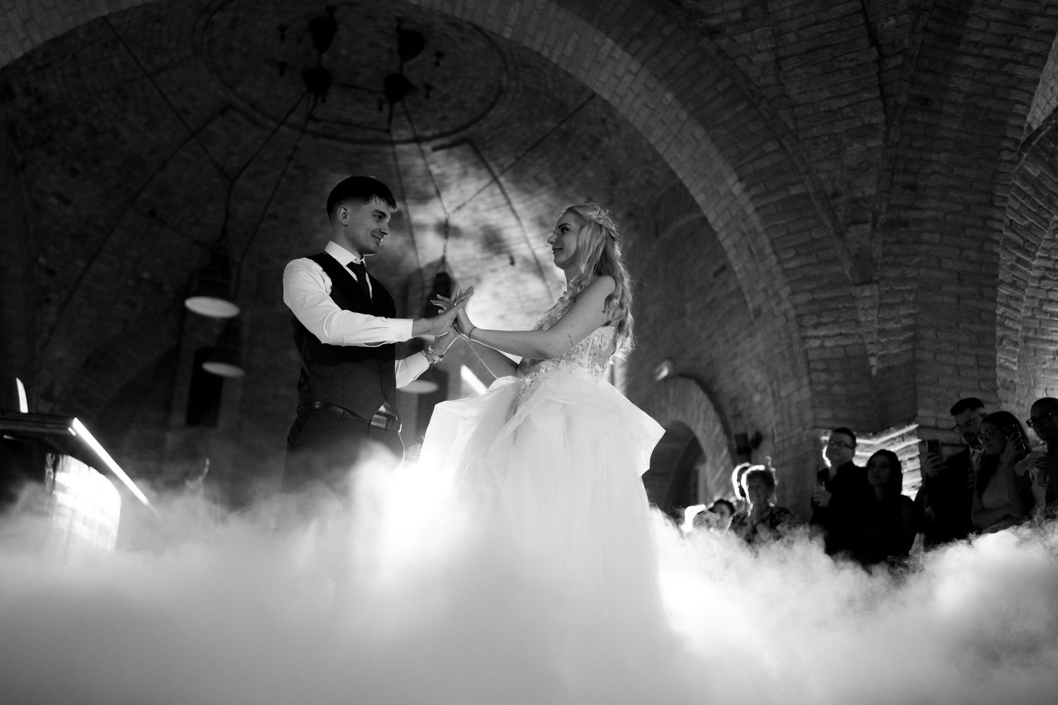 Two people share a romantic dance surrounded by atmospheric fog during what appears to be a formal celebration.