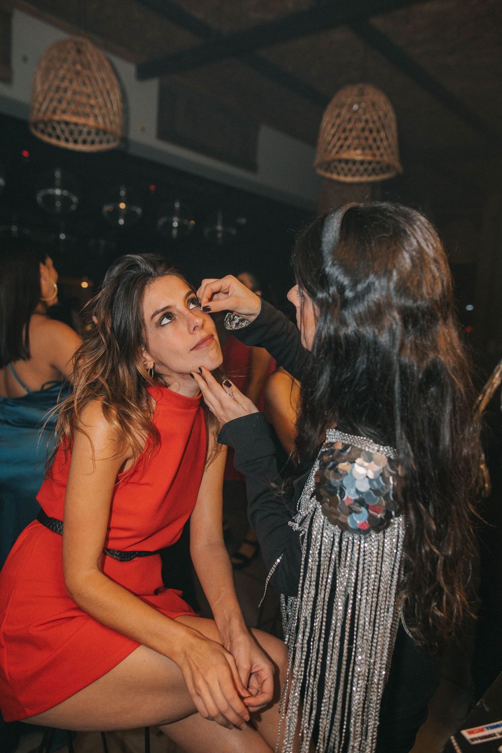 Escena elegante de evento con lámparas de mimbre colgantes y personas preparándose, ideal para stand de glitter y glitter bar para fiestas.