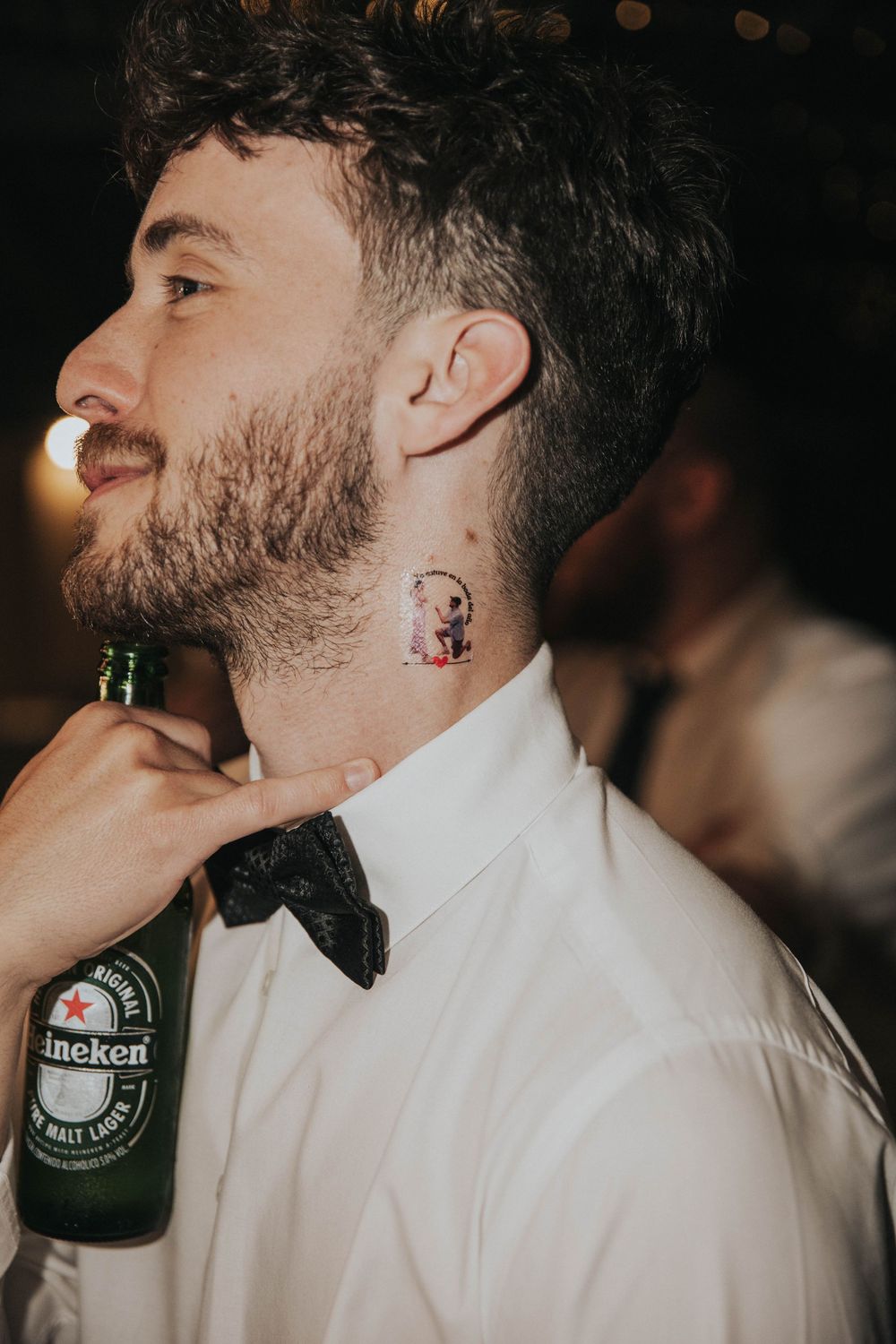 Una hombre con camisa blanca mostrando un tatuaje en el cuello que se puso en el stand de glitter