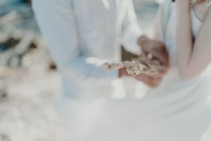 Bride picking wildflowers from rocks — unscripted beach elopement detail.