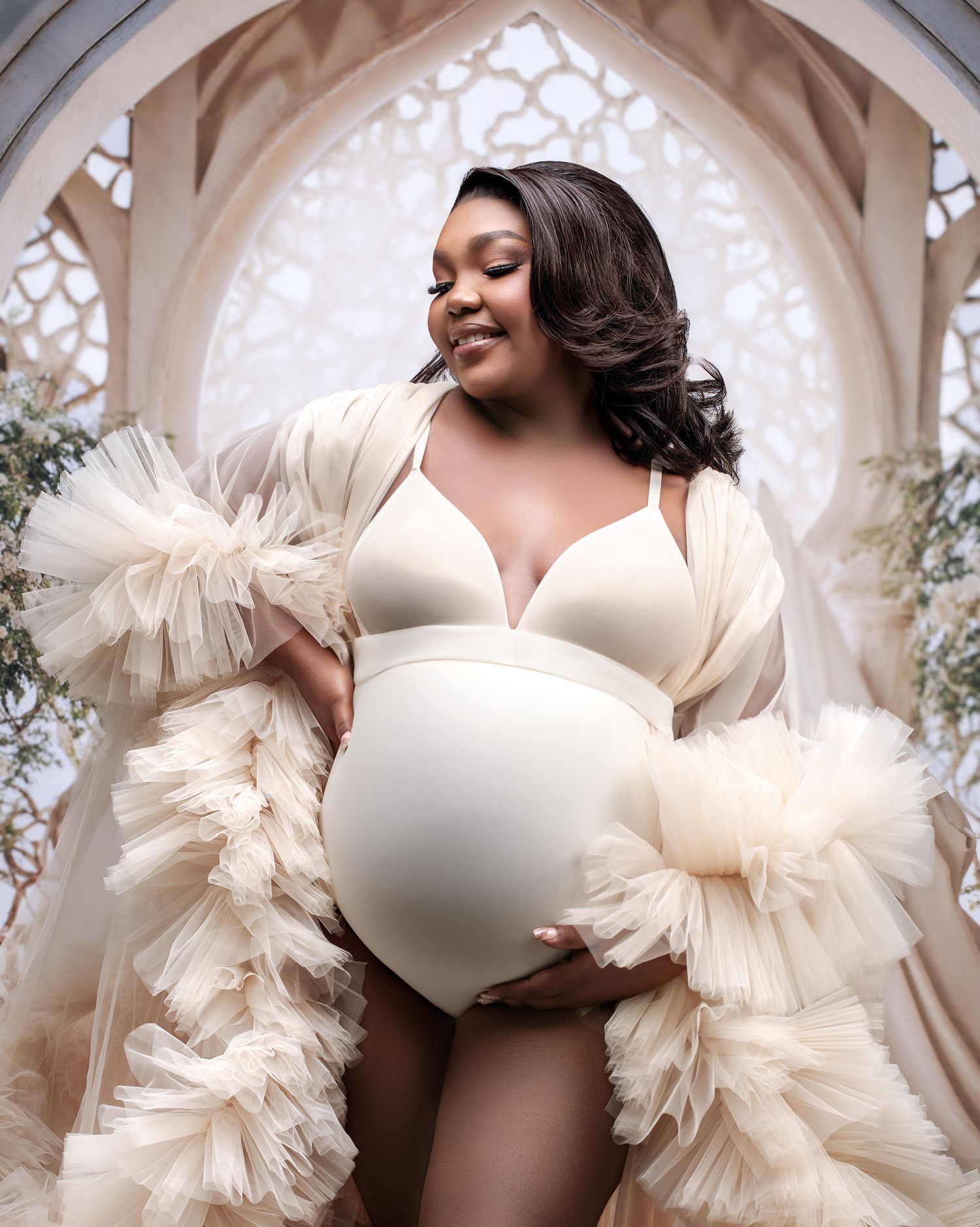 Close up shot of a pregnant mother holding her belly in cream bodysuit and tulle robe.