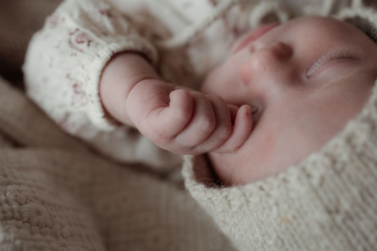 A tiny infant's hand rests against soft white fabric with delicate floral patterns.