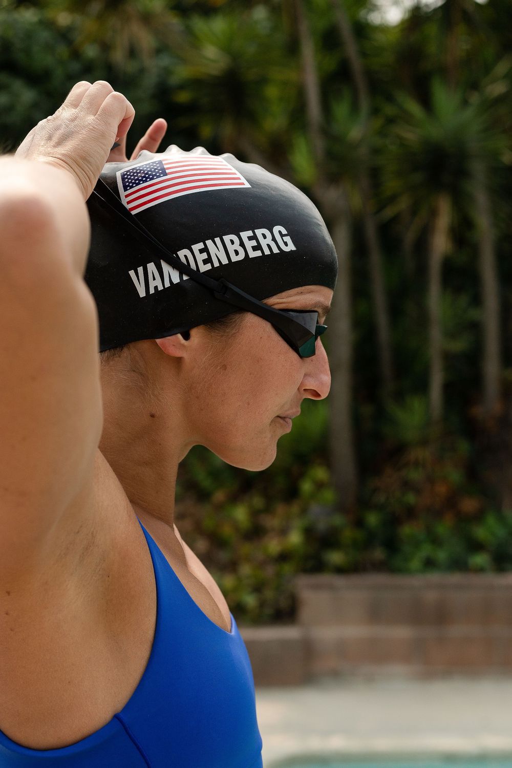 Swimmer adjusts Vandenberg cap and goggles before pool training — athletic portrait by Adrian Rudd Kahn.