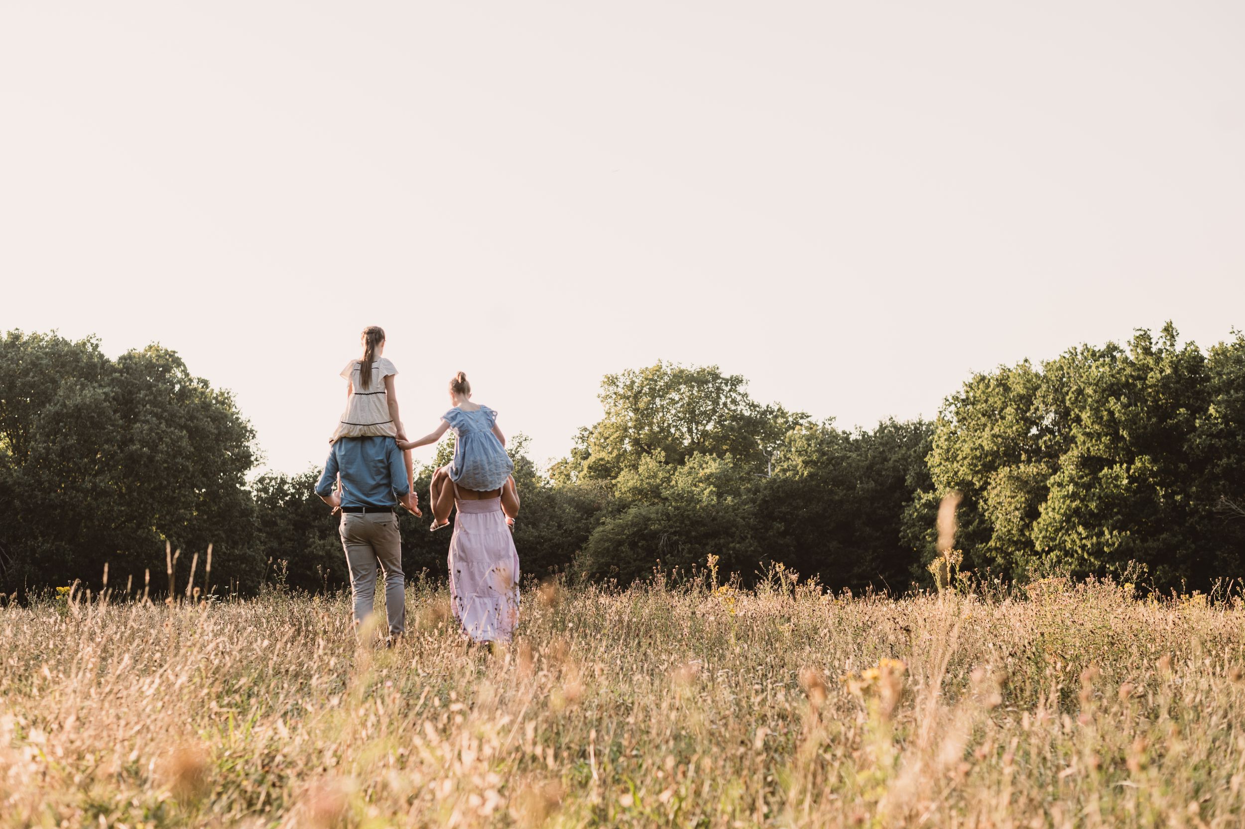 A family walking through a golden summer meadow at sunset as warm light illuminates the tall grass.