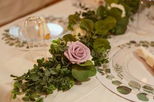 Elegant table setting with fresh eucalyptus garland and pale pink rose centerpiece on white linens.