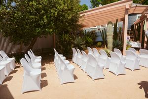 White ceremony chairs arranged in rows outdoors under a pergola with desert landscaping.