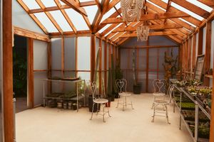 Interior of a rustic wooden greenhouse with metal chairs and translucent panels letting in natural light.
