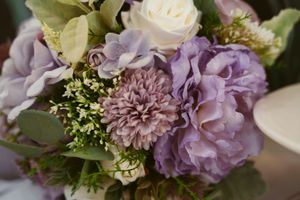 A romantic floral arrangement with purple and white blooms including dahlias, roses, and delicate greenery.