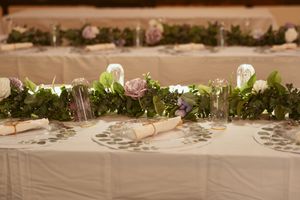 Elegant table setting with floral garland centerpiece and white linens for wedding reception.