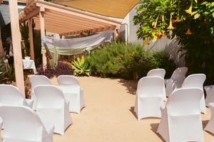 Outdoor ceremony space with white chairs and fabric canopy in a garden setting.