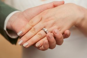 Close-up of hands displaying an engagement ring with a white manicure.