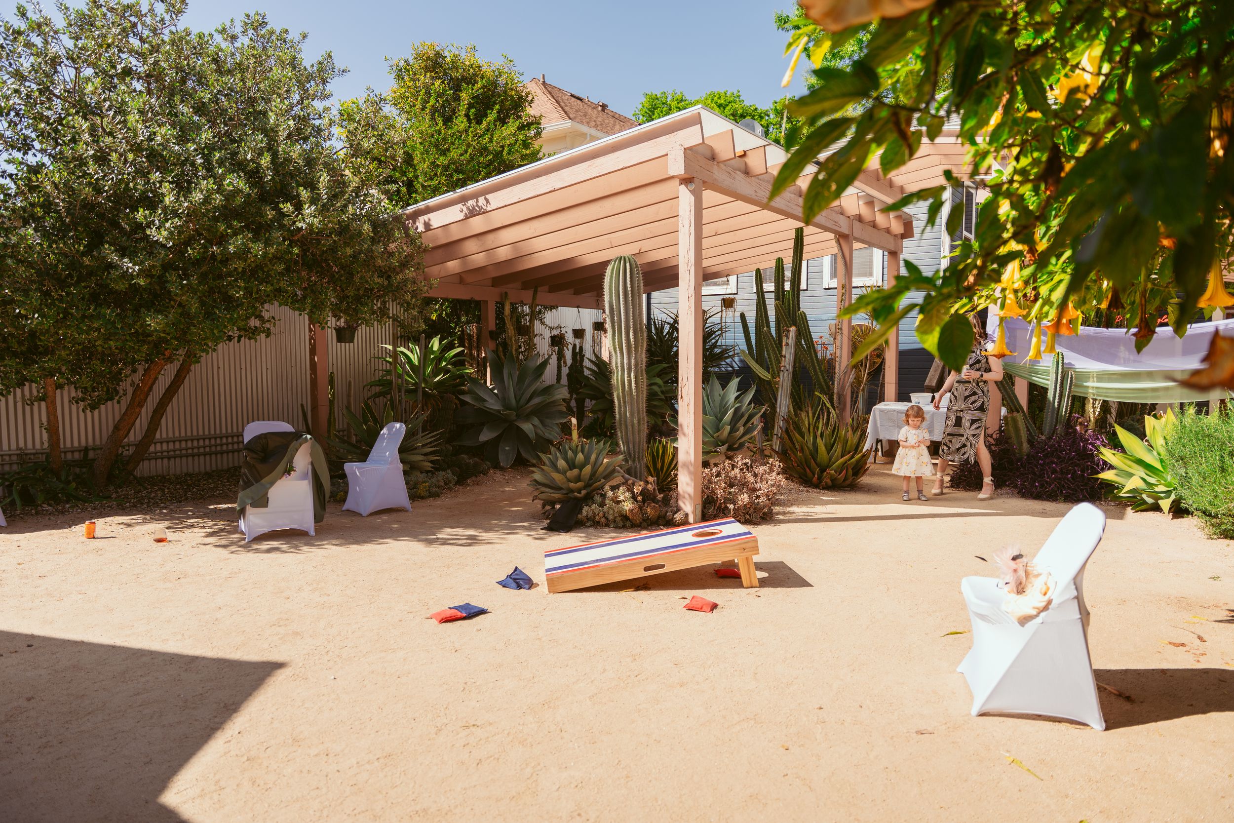 Outdoor wedding venue with white chairs and pergola under bright sunlight.