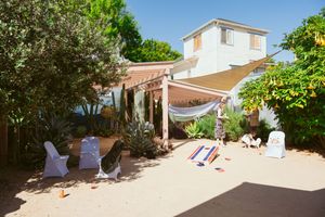Outdoor wedding setup with white chairs and pergola in a sunny backyard garden setting.