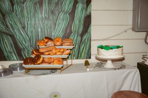 Dessert table with pastries and cake displayed against a green botanical backdrop.