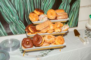 Three-tiered platter filled with assorted donuts and pastries on a white tablecloth.