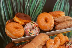 Assorted glazed and sprinkle-topped donuts displayed on a platter with tropical palm leaves.