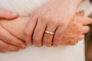 Closeup of hands with a gold wedding band ring on white fabric background.