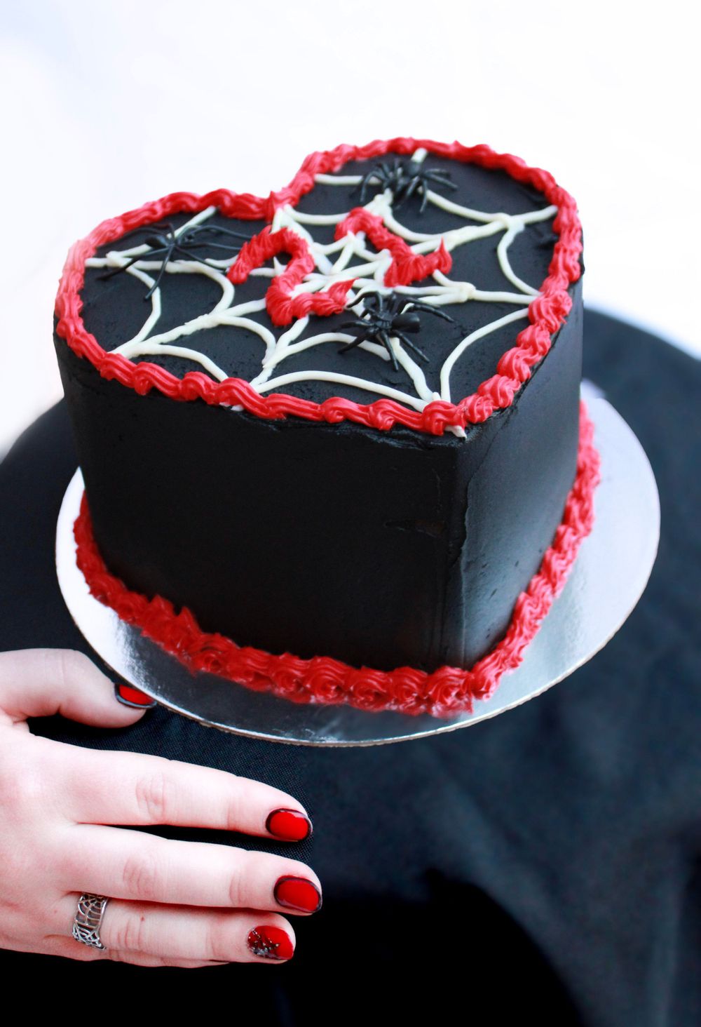 Heart cake with spider web design and red-painted nails visible in frame.
