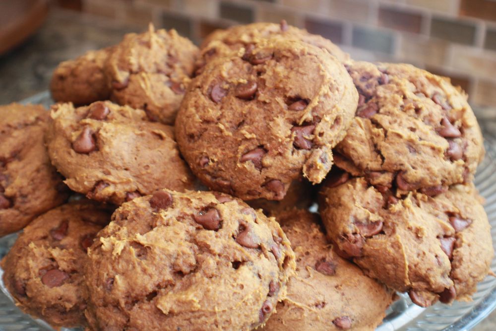 Fresh baked chocolate chip cookies displayed on crystal plate with rustic brick background.