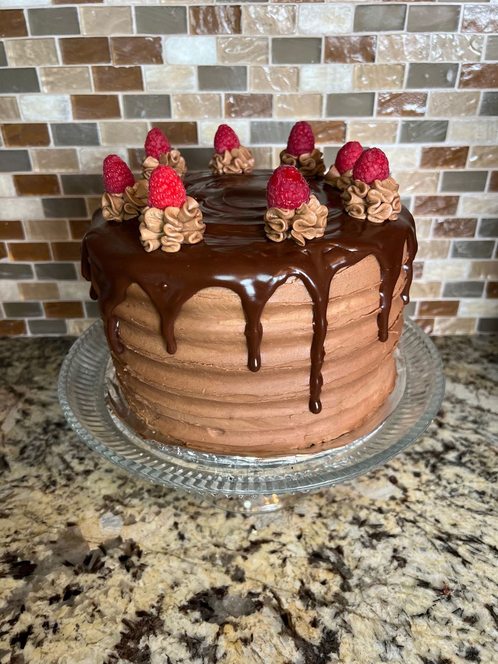 Chocolate layer cake with ganache drip and fresh raspberries on top.