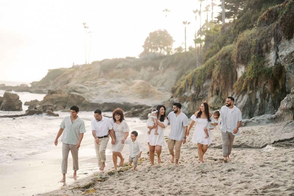A group of people in white outfits walking together on a scenic beach at sunset with coastal cliffs in the background.