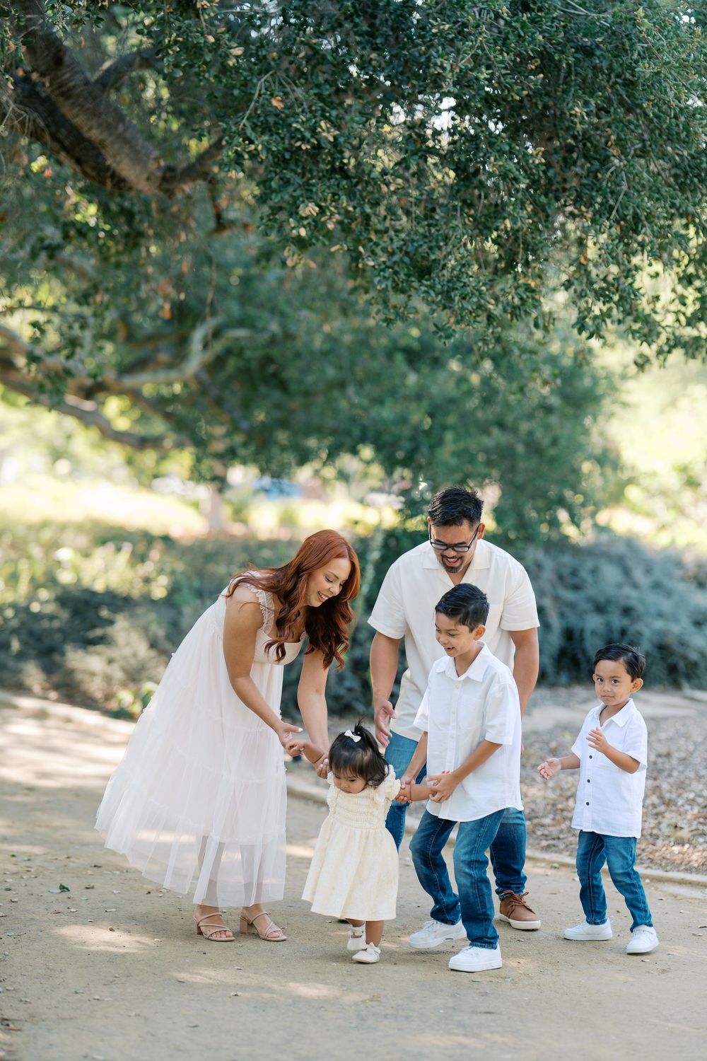A family shares playful moments together on a dirt path surrounded by lush green trees.