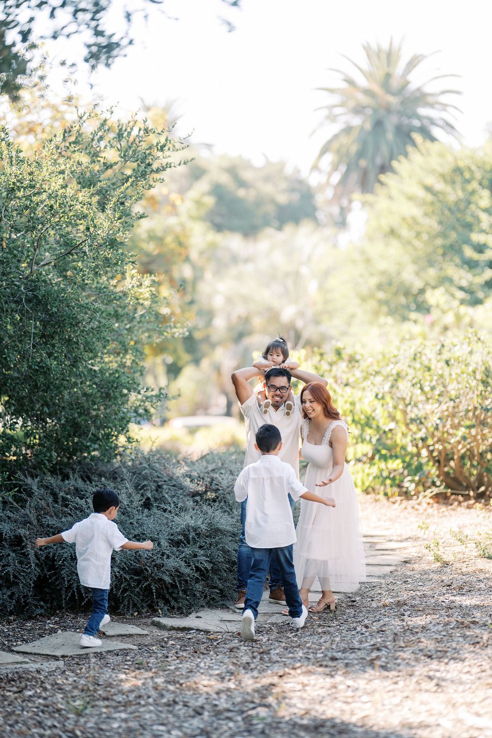 Family enjoys a playful moment together on a sunlit path surrounded by lush greenery.