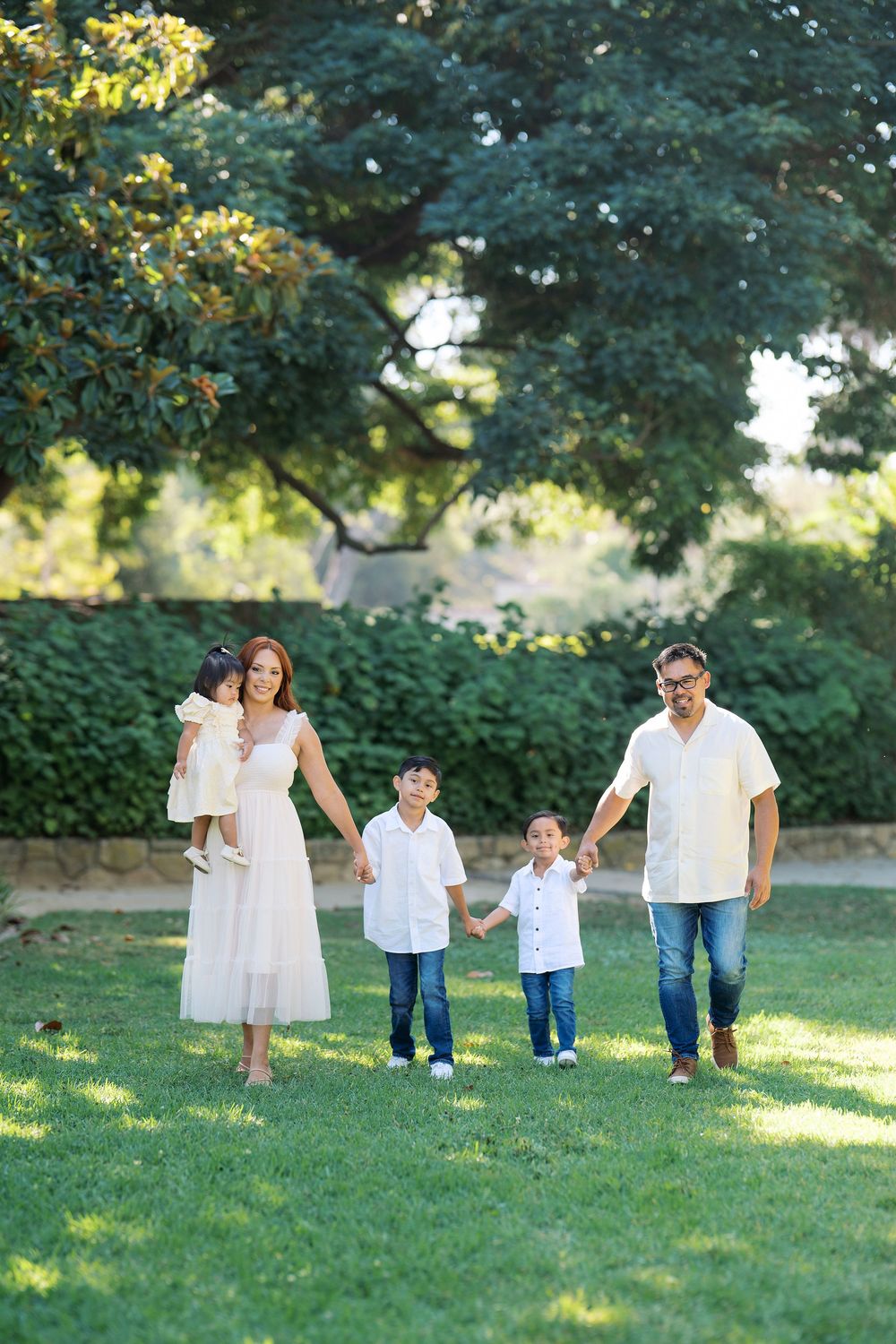 Family in white outfits playing together on a grassy lawn during a summer photo session.