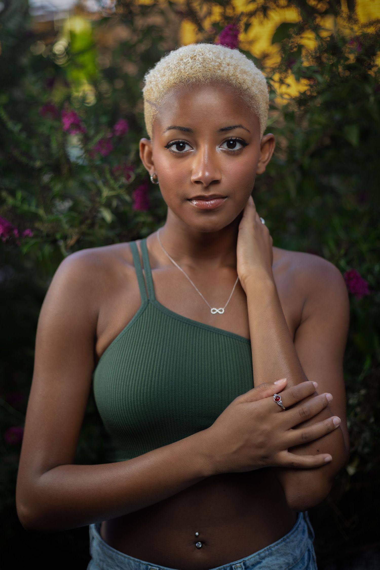 Portrait of woman in green tank top with blonde hair against colorful garden background.