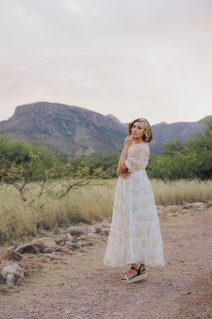 A flowing white floral dress twirls against a desert mountain backdrop with desert brush and rocks.