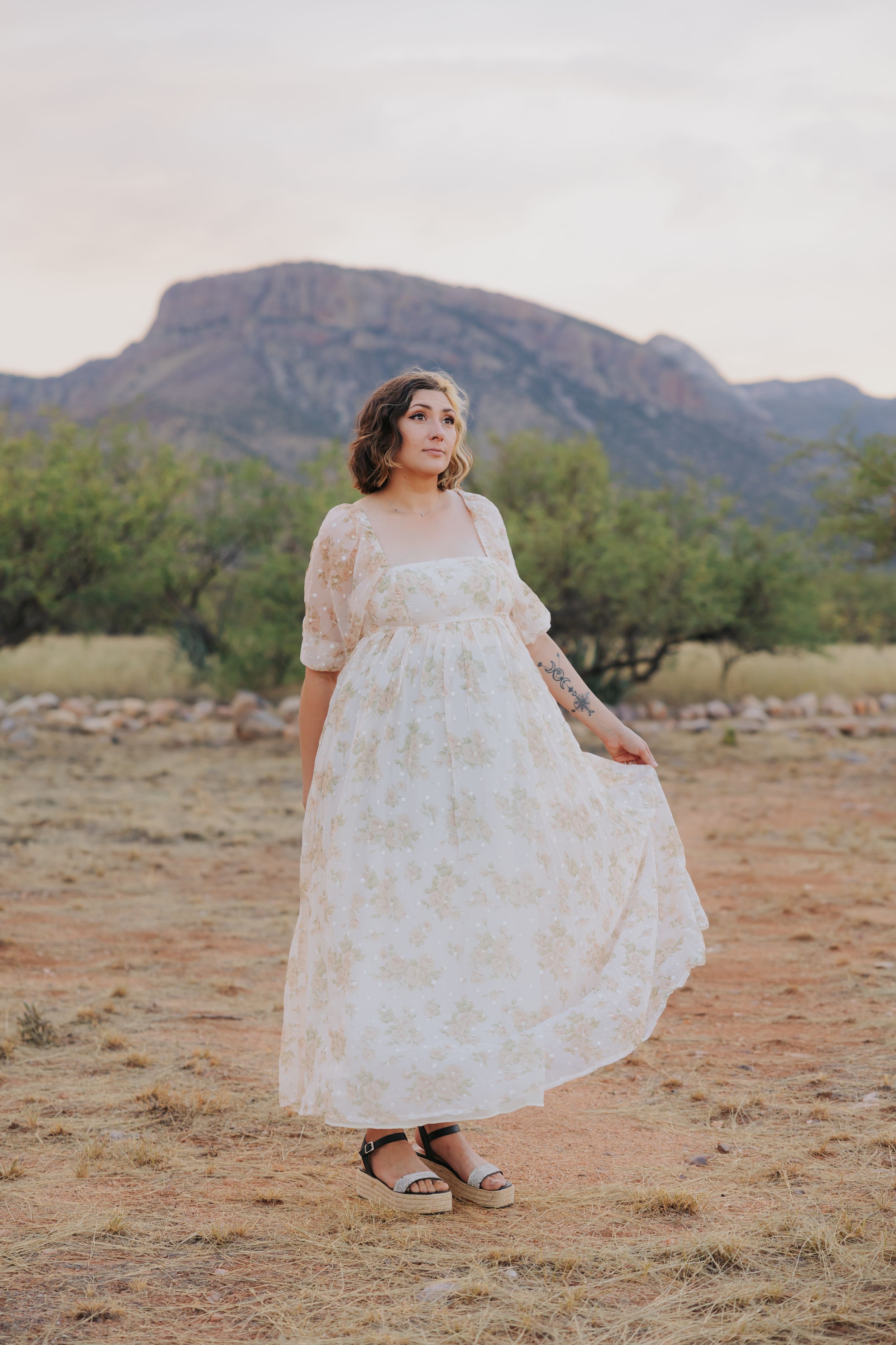 A flowing white floral dress dances in the desert breeze against mountainous terrain.
