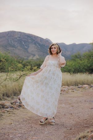 Playful twirling motion in white floral dress captured against desert mountain scenery.