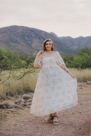 White floral dress catches desert light while dancing against mountain landscape.