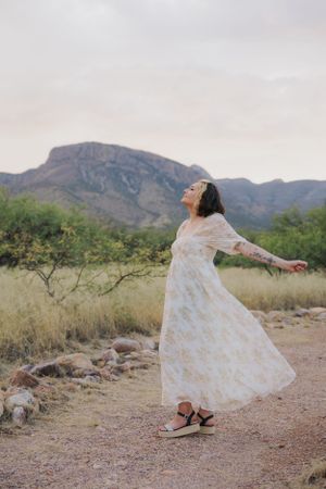 Joyful dance movements in white dress captured against desert mountain backdrop.