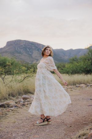 A flowing white floral dress twirls against a desert mountain backdrop during a sunset photoshoot.