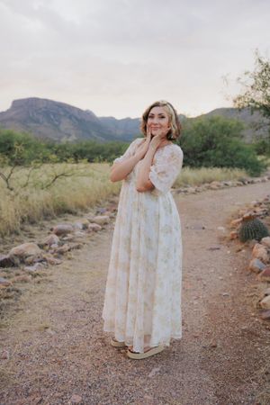 Standing on a desert trail in a delicate white dress with mountains in the distance.