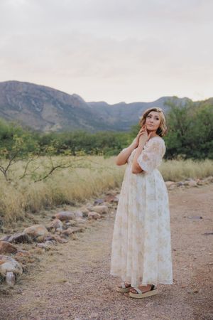 Ethereal pose in a flowing white dress on a desert path with mountain views.