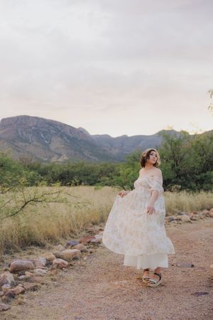Dancing in a white floral maxi dress on a desert trail with mountain vistas.