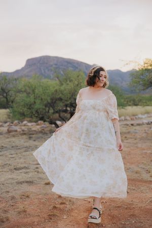 A delicate floral dress twirls in the desert setting with mountains and brush in the background.